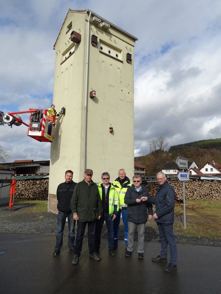 (von rechts nach links) Matthias Hahner (Geschäftsführer der OsthessenNetz GmbH) übergibt Peter Paul (1. Bürgermeister von Mittelsinn) den Schlüssel zur umfunktionierten Turmstation; daneben Bernd Christ (Monteur ServiceCenter Süd der OsthessenNetz GmbH), Hans-Michael Schäfer (Sachgebietsleiter ServiceCenter Süd der OsthessenNetz GmbH), Naturschützer und Ornithologe Armin Welzenbach, und Torsten Weigand (Baukoordinator ServiceCenter Süd der OsthessenNetz GmbH). Im Hintergrund bringt Heribert Reißer (Monteur ServiceCenter Süd der OsthessenNetz GmbH) einen Vogelkasten an.