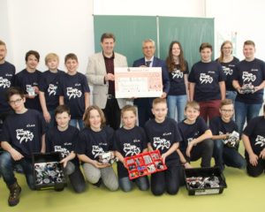 L.A.N. Geschäftsführer Esmail Akbari überreicht den Scheck an Schulleiter Marco Schumacher. Auf dem Bild sind auch die Schüler der Roboter AG und die betreuenden Lehrer zu sehen.