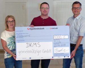 Theresa Kümmel, Mitarbeiterin der JUMO-Marketingabteilung (links) und Marketingleiter Michael Diegelmann (rechts) übergeben den symbolischen Scheck in den Räumen der JUMO GmbH & Co. KG an den DKMS-Vertreter Michael Möller.